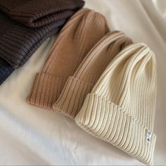 three beanies laying on top of a bed next to each other in different colors