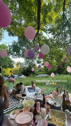 people are sitting at a picnic table with pink and white balloons hanging from the trees