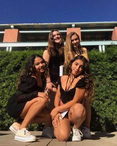 four girls are posing for the camera in front of some bushes