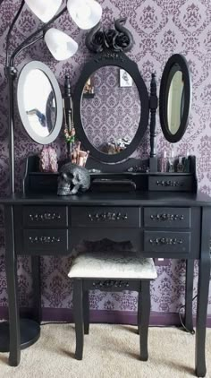 a black vanity with two mirrors and a stool in front of purple damask wallpaper