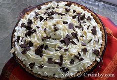 a pie with white frosting and chocolate chips on top sitting on a red cloth