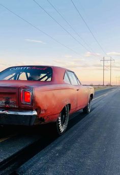 an old red car is parked on the side of the road with power lines in the background