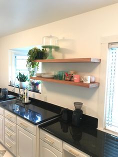 a kitchen with white cabinets and black counter tops, along with shelves above the sink