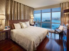 a bedroom with a large window overlooking the water and cityscape is pictured in this image