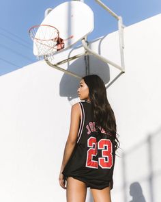 a woman standing in front of a basketball hoop with her back turned to the camera