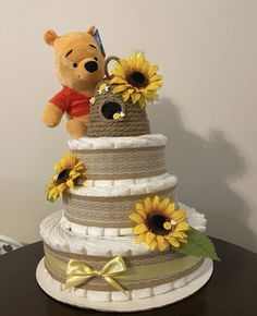 a teddy bear is sitting on top of a tiered cake with sunflowers