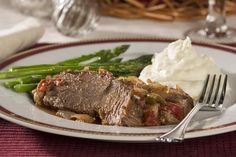 a white plate topped with meat and mashed potatoes next to asparagus on a table