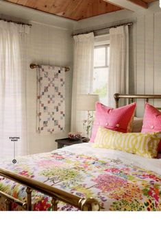 a bed with colorful pillows and quilts on the covers in a room that has white walls