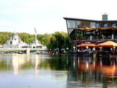 people sitting at tables on the edge of a lake in front of a large building