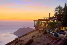 a house sitting on top of a hill next to the ocean at sunset or dawn