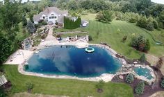 an aerial view of a large pool surrounded by lush green trees and lawns, with a house in the background