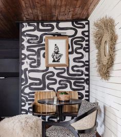 two chairs and a table in front of a wall with black and white designs on it