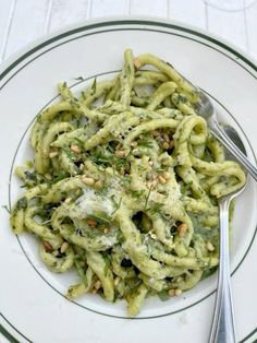 a white plate topped with pasta covered in pesto and pine nuts next to a fork