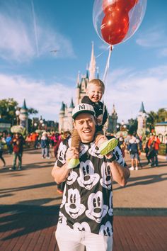 a man holding a child in front of a castle with a red balloon attached to it