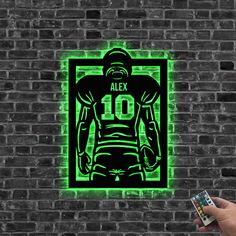 a hand holding a remote control in front of a brick wall with an image of a football player on it