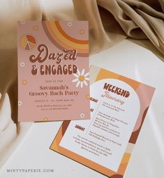 an orange and pink wedding card on top of a white table cloth next to it