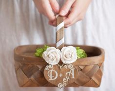 a person is holding a small cake in a basket with flowers and initials on it