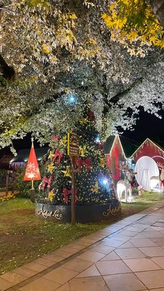 a christmas tree is lit up in front of a red barn and trees with white lights