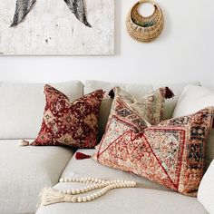 a white couch with pillows on top of it next to a painting and beaded necklace