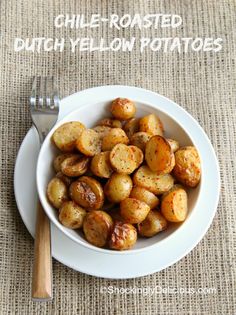 a white bowl filled with cooked potatoes on top of a table next to a fork