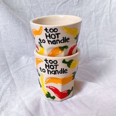 two ceramic cups with colorful peppers painted on them, one has the words too hot to handle