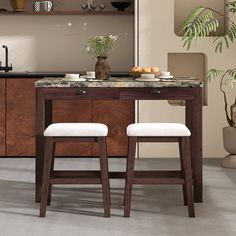 two stools sit in front of a kitchen island with marble top and wooden legs