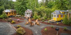 several tiny houses in the woods surrounded by trees and gravel, with one person sitting at a table