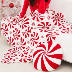 a woman in red and white crocheted blanket next to a christmas tree on the floor