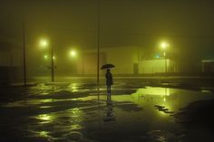 a person holding an umbrella standing in the rain at night with street lights behind them