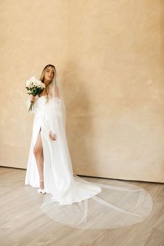 a woman in a white wedding dress holding a bouquet and standing on a wooden floor