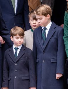 two young boys in suits and ties stand next to each other as people look on