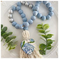 a white plate topped with blue beads and a tasseled heart pendant next to green leaves