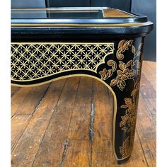 an ornate black and gold painted table on wooden floor