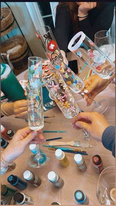 several people are holding up wine glasses on a table covered with bottles and paintbrushes