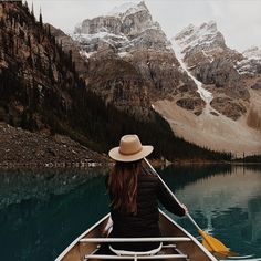 a woman in a hat is paddling a canoe on the water with mountains in the background