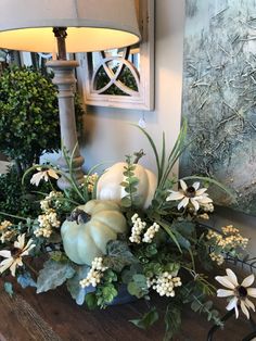 a wooden table topped with white pumpkins and greenery