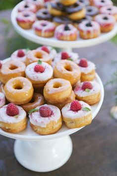 there are many doughnuts on the cake plate and one is topped with raspberries