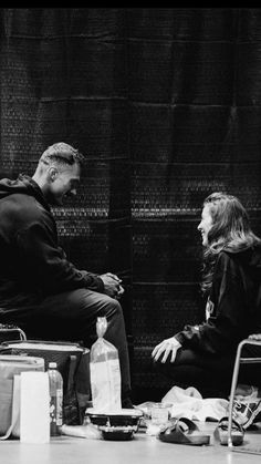 black and white photograph of two people sitting next to each other in front of a wall