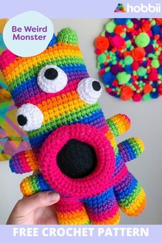 a hand holding a colorful crocheted stuffed animal in front of a wall with the words be weird monster on it