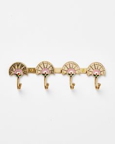 three gold and pink brooches are hanging on a white wall, one is in the shape of an umbrella