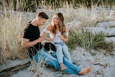 a man and woman sitting on the sand with a dog in their lap looking at each other