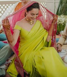 a woman in a yellow sari sitting on the ground with two men behind her