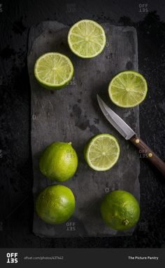 limes and a knife on a cutting board with a black slate surface, top view