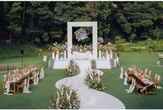 an outdoor wedding setup with tables and chairs set up in the grass, surrounded by greenery