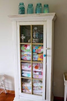 an old cabinet is filled with quilts and jars