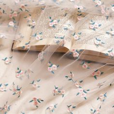 an open book with flowers on it sitting on top of a white cloth covered table