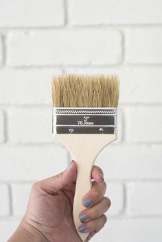 a hand holding a paint brush in front of a brick wall