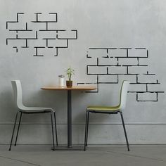 two chairs sitting at a table in front of a wall with a plant on it