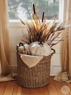 a wicker basket filled with pumpkins and other fall decorations in front of a window