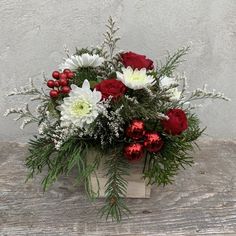 a vase filled with white and red flowers on top of a wooden table next to a wall